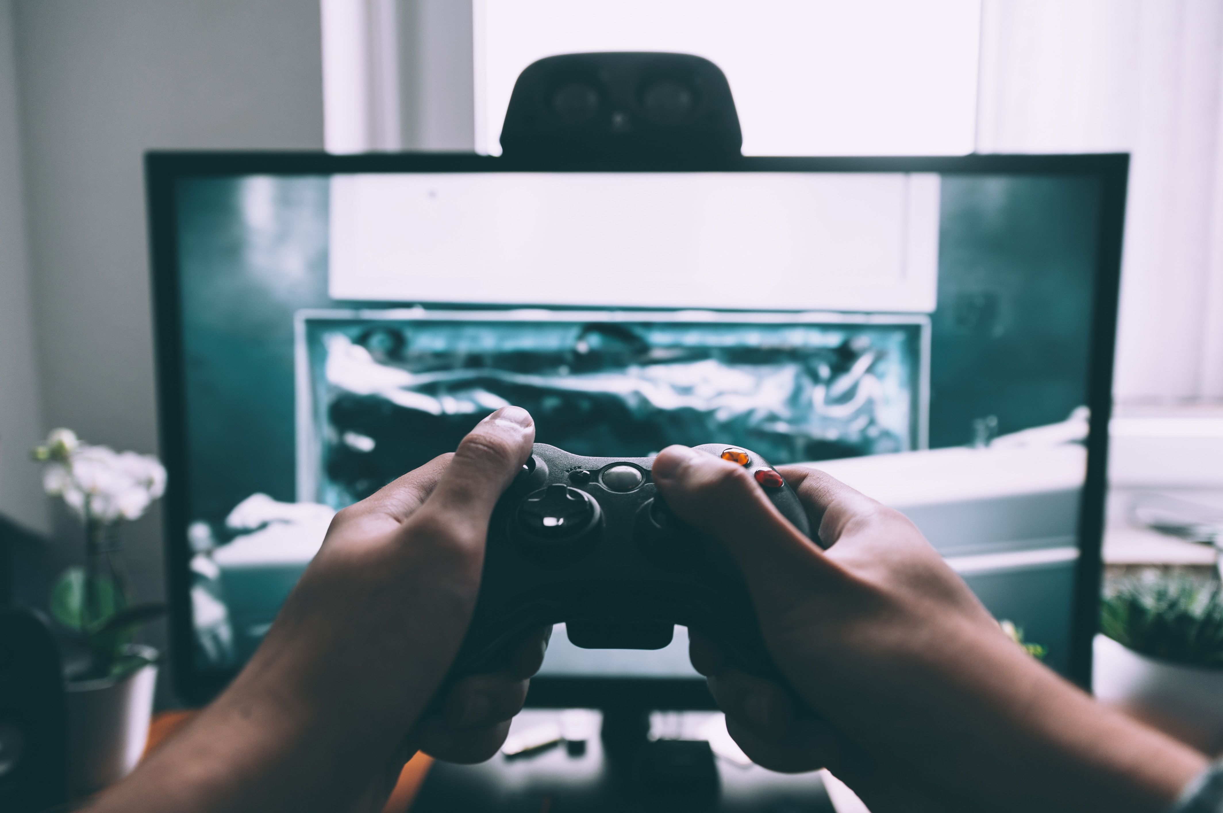 Two hands holding a game controller in front of tv screen.